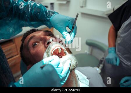 Caucasian male client sitting in dentist chair while nurse operates on teeth Stock Photo