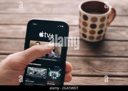 Young man chooses a series or a movie in the Apple TV service on a smartphone during coffee break. Stock Photo