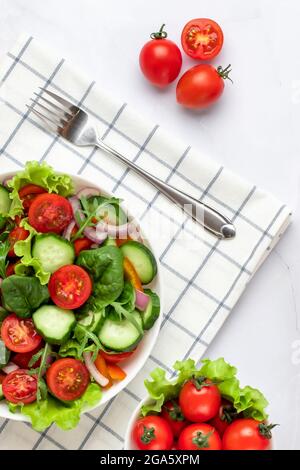 Vegetables on a white plate on a gray marble background. Top view. Salad made with cherry tomatoes, cucumbers, arugula, basil and dressed with olive o Stock Photo