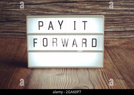 Lightbox with Pay it forward text message on wooden background Stock Photo