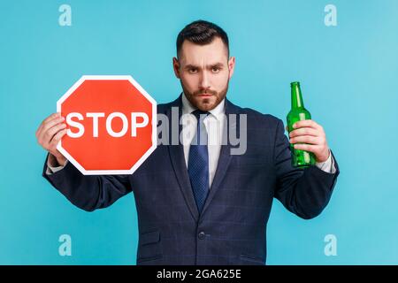 Stop drinking alcohol. Do not drive drunk. Anxious businessman showing alcoholic beverage beer bottle and stop sign, warning and worrying. Indoor stud Stock Photo