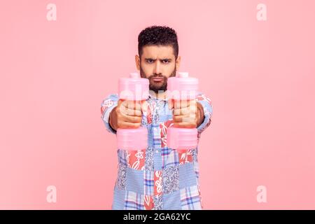 Portrait of funny strong man wearing blue casual style style shirt training biceps and triceps with rose dumbbells, looking at camera, showing power. Stock Photo