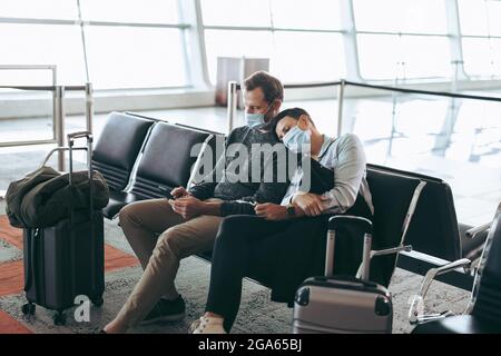 traveler couple in pandemic waiting at airport terminal. Man and woman in face masks sitting at airport waiting area. Stock Photo