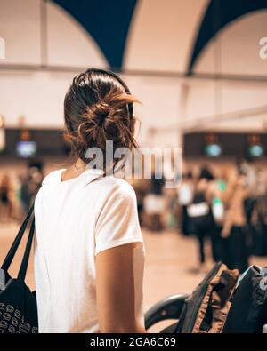 Caucasian woman going into the airport terminal during the covid pandemic loading her luggage onto a trolley while watching the long queue to check-in Stock Photo