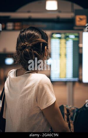 Caucasian girl going into the airport during the covid pandemic loading her luggage into a trolley while looking at her check-in desk - epidemic time Stock Photo