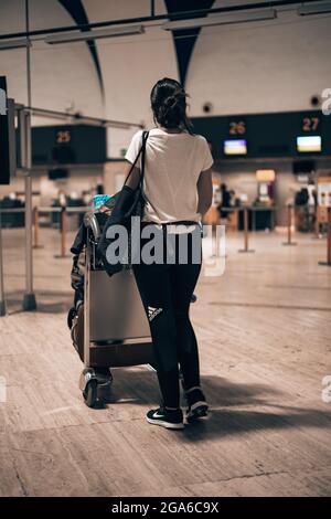 Woman walking through the airport terminal during the covid pandemic loading her luggage into a trolley walking through the terminal corridors Stock Photo