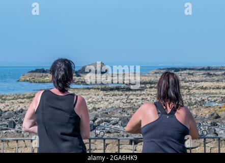 two female friends at the seaside looking out over the water chatting at dunure harbour in ayrshire on the scottish coast. Stock Photo