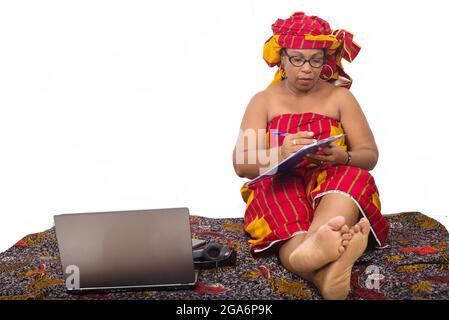 mature woman in loincloth sitting on the floor writing on her note pad. Stock Photo