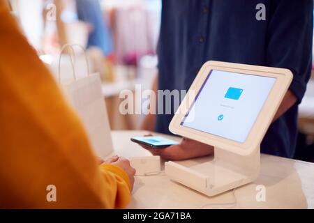Close Up Of Sales Assistant Accepting Contactless Payment In Shop From Customer Using Mobile Phone Stock Photo