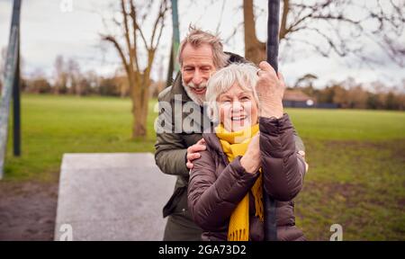 Senior Couple Having Fun Playing On Swing In Park Playground Stock Photo