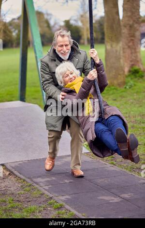 Senior Couple Having Fun Playing On Swing In Park Playground Stock Photo