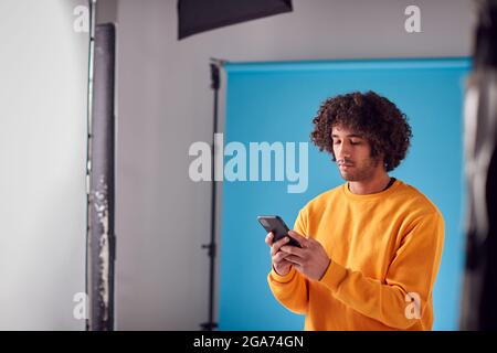 Studio Portrait Of Young Man Looking At Mobile Phone Against Blue Background Stock Photo