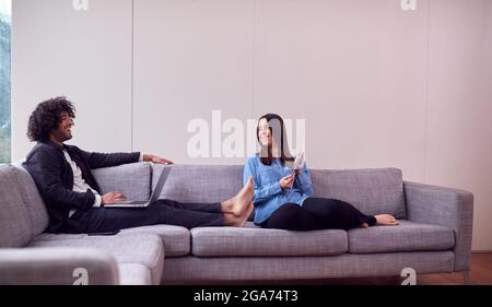 Relaxed Young Couple At Home Sitting On Sofa Using Digital Tablet And Laptop Computer Stock Photo