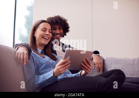 Relaxed Young Couple At Home Lying On Sofa Streaming Movie To Digital Tablet Stock Photo