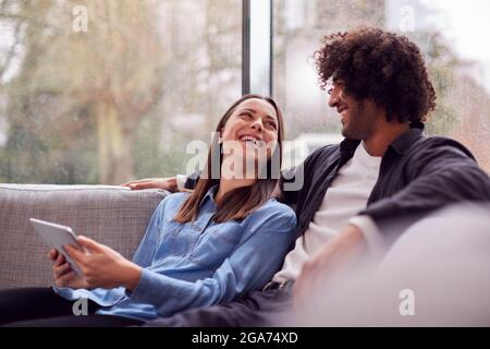 Relaxed Young Couple At Home Lying On Sofa With Digital Tablet Stock Photo