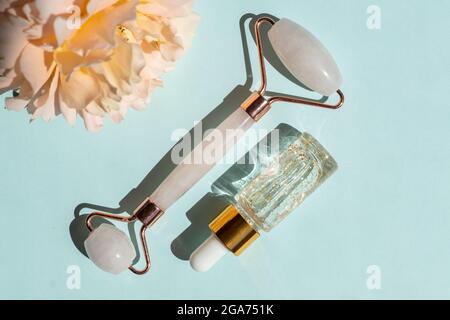 Massage roller for the face made of rose quartz with bottle of 24k gold serum on a blue background. The concept of skin care at home Stock Photo