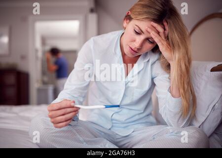 Unhappy Woman Wearing Pyjamas In Bedroom Holding Pregnancy Test Stock Photo