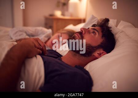 Couple With Man Lying In Bed Awake At Night Suffering With Insomnia Stock Photo