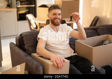 Man sitting on sofa and showing key of new home Stock Photo