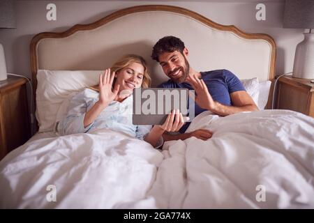 Couple Lying In Bed In Morning Having Video Call On  Digital Tablet Stock Photo