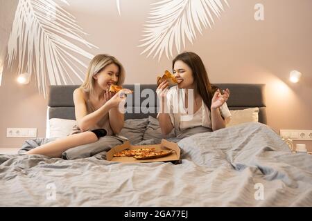 Happy european women lying on bed and eating pizza Stock Photo