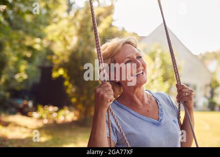 Carefree Smiling Retired Woman Having Fun On Garden Swing Stock Photo