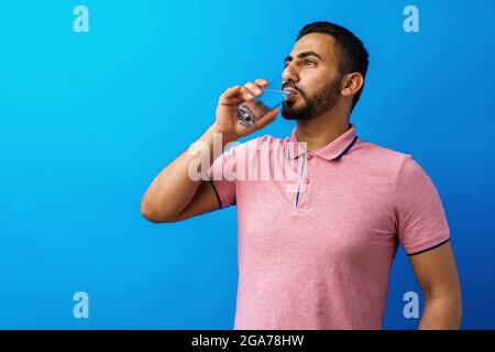 Handsome hispanic man drinking a glass of fresh water against blue background Stock Photo