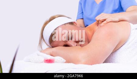 Specialist making shoulder massage to an adult woman relaxed and lying with closed eyes in a beauty salon . Stock Photo