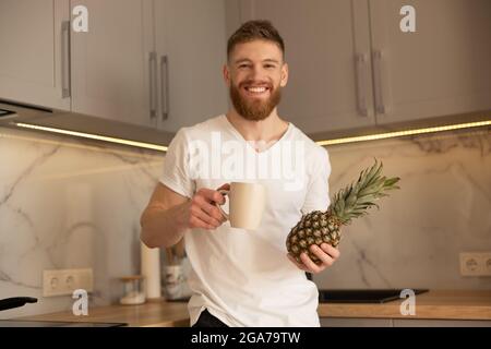 Man drinking tea from cup and holding pineapple Stock Photo