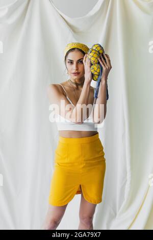 pretty woman in yellow headscarf and crop top holding string bag with lemons on white Stock Photo