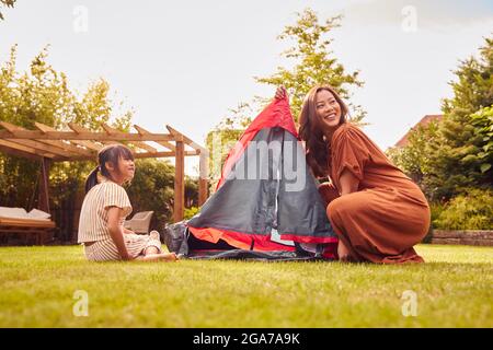 Asian Mother With Daughter In Garden At Home Putting Up Tent For Camping Trip Together Stock Photo