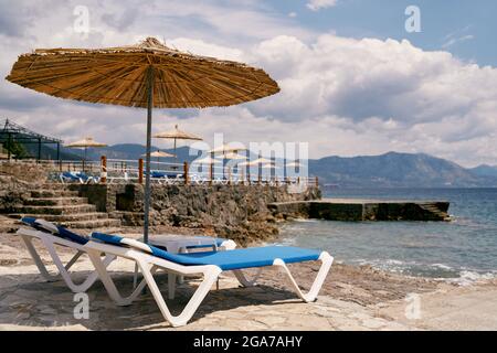 Sun loungers stand under a beach umbrella near water Stock Photo