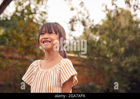 Portrait Of Smiling Asian Girl With Missing Front Teeth Having Fun In Garden At Home Stock Photo