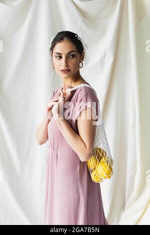 brunette woman holding reusable string bag with lemons on white Stock Photo