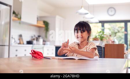 Young Asian Girl Home Schooling Working At Table In Kitchen Counting On Fingers Stock Photo