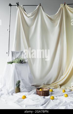 fresh lemons in wicker basket near pineapple on white bed sheets near bouquet of flowers Stock Photo