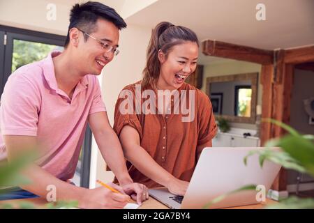 Smiling Couple Sitting At Table At Home Reviewing Domestic Finances Using Laptop Stock Photo