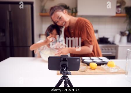 Asian Mother And Daughter Baking Cupcakes In Kitchen At Home Whilst On Vlogging On Mobile Phone Stock Photo