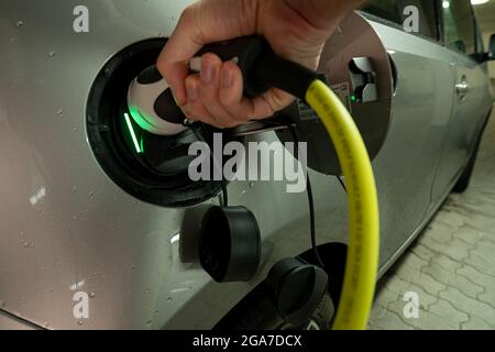 Hands on the charging wire of an e-car with an active charging process, shown by the green light. Stock Photo