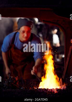 Female Blacksmith Heating Metalwork In Flames Of Forge Stock Photo
