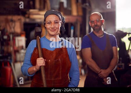 Portrait Of Male And Female Blacksmiths Holding Tools Standing In Forge Stock Photo