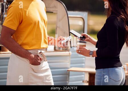 Male Customer Making Contactless Payment Using Mobile Phone At Mobile Coffee Van Stock Photo