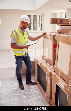 Builder Wearing Hard Hat With Clipboard Checking Delivery Of New Kitchen Units Inside Property Stock Photo