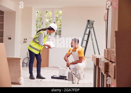 Female Surveyor With Clipboard Meeting With Decorator Working Inside Property Stock Photo