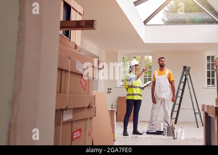 Female Surveyor With Clipboard Meeting With Decorator Working Inside Property Stock Photo