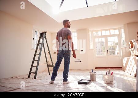 Rear View Of Man Holding Paint Roller Decorating New Home Stock Photo