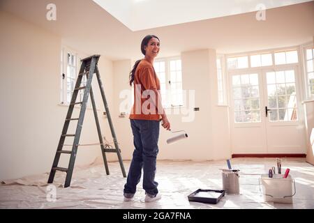 Rear View Of Woman With Paint Roller Decorating New Home Stock Photo