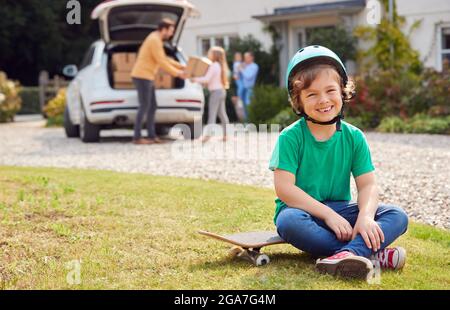 Portrait Of Boy With Skateboard Outside New Family Home On Moving Day Unloading Boxes From Car Stock Photo