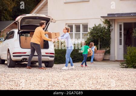 Family Outside New Home On Moving Day Loading Or Unloading Boxes From Car Stock Photo