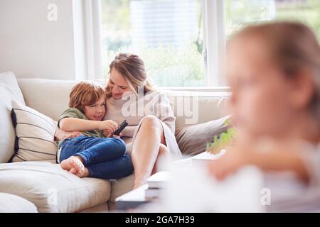 Mother Relaxing With Children On Sofa At Home Watching TV Together Stock Photo